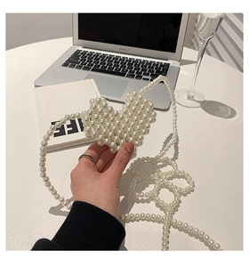 Close-up of heart-shaped pearl woven crossbody bag on a desk with elegant props
