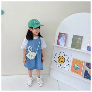 Detail of girl wearing blue denim vest dress with green cap and pearl beaded handbag