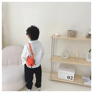 Detail of a bright orange mini canvas crossbody bag for kids with black nylon strap