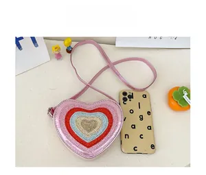 Size comparison of pink heart-shaped sequin crossbody bag next to a mobile phone