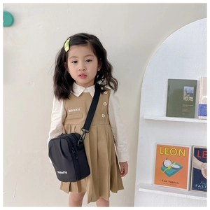 Detail shot of a black nylon crossbody bag paired with a khaki vest dress for kids