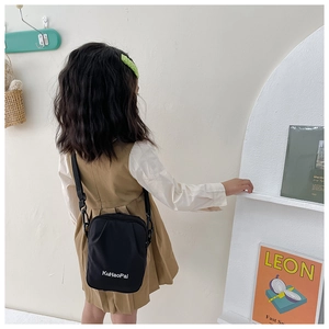 Detail of child wearing black canvas crossbody bag with white KuHaoPai brand lettering