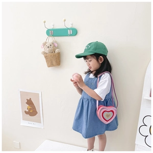 Detail of pink heart-shaped sequin crossbody bag worn by child with denim overall