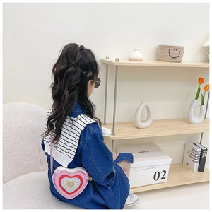 Toddler girl wearing pink sequin heart-shaped crossbody bag over blue denim dress