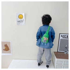 Detail view of a child wearing a green cartoon bear crossbody bag in a lifestyle setting