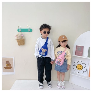 Detail of blue and pink cartoon bear chest bags worn by kids in a stylish indoor setting