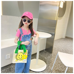 Detailed view of child fashion outfit featuring a yellow smiley face canvas messenger bag