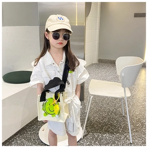 Close-up of kids canvas tote bag with green smiley face and floral charm accessory