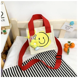 Detail view of smiley canvas tote with red straps and flower charm on a striped blanket