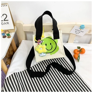 Detail of white canvas tote bag featuring green smiley face print and yellow flower charm