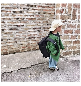 Outdoor street style detail of a green work jacket, black backpack, and beige baseball cap