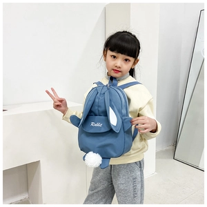 Detailed view of kids blue canvas backpack with rabbit ears and plush pendant on model