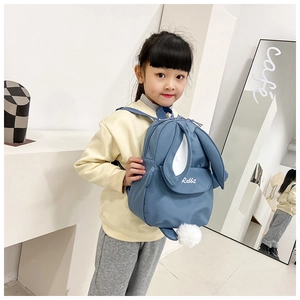Detail view of a blue kids backpack with cute rabbit ears and a white plush pompom tail