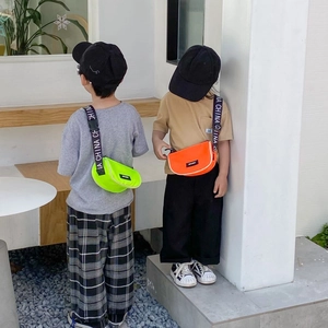 Gros plan sur des sacs bandoulière enfant en toile vert néon et orange avec sangles sport