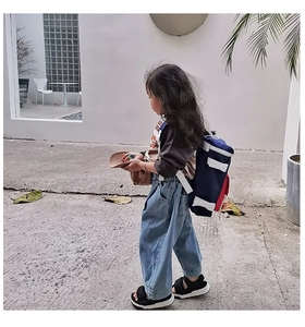 Outdoor side view of a child wearing a lightweight navy and red nylon backpack