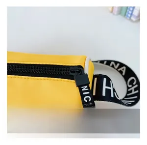 Détail d'une pochette en toile jaune avec fermeture éclair noire et sangle à lettres NICE