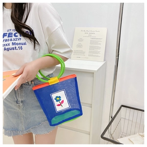 Detail of blue mesh bucket bag with green handles and white flower embroidery patch