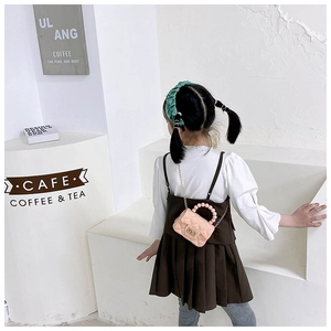 Detail of pink quilted girl's bag with pearl handle and metal chain strap in cafe setting