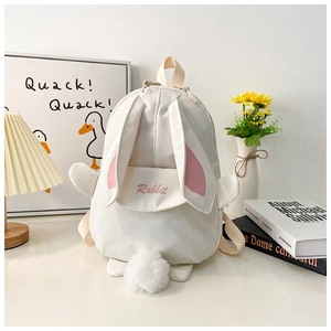 Cute white cartoon rabbit backpack with long ears and plush tail on a minimalist desk