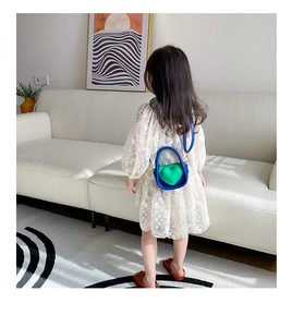 Détail du mini sac cœur bleu et vert pour fille porté par un enfant en robe de dentelle