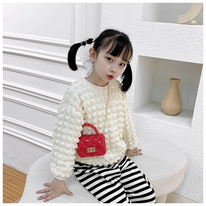 Detail of red quilted PVC jelly bag with pearl handle worn by a girl in cream sweater