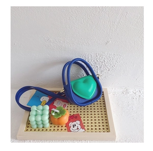Détail d'un mini sac cœur bicolore bleu marine et vert posé sur un plateau en rotin