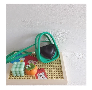 Détail du mini sac à main vert avec rabat en forme de cœur marron sur un plateau tressé