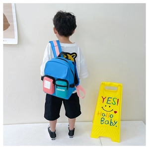 Children's colorful backpack worn by a kid model against a minimal wall background