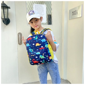 Detail of navy cartoon dinosaur backpack featuring a yellow side mesh pocket and zip pouch