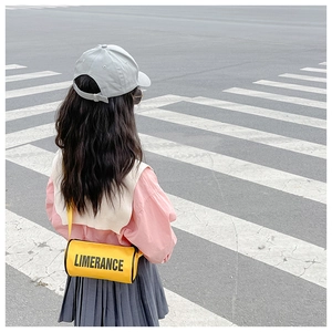 Gros plan d'un enfant portant un sac bandoulière cylindrique jaune vif avec lettrage noir