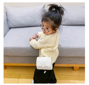 Girl wearing a white quilted crossbody bag with heart buckle and gold chain strap
