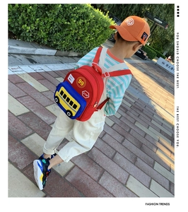 Toddler walking outdoors wearing a red backpack with a yellow 3D bus-shaped pocket