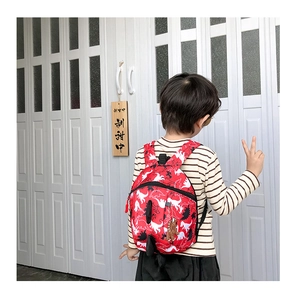 Rear view of a red children's dinosaur print backpack with adjustable straps and tail detail