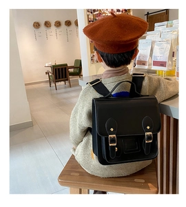 Detail of vintage black PU leather kids backpack with golden buckles in a cafe setting