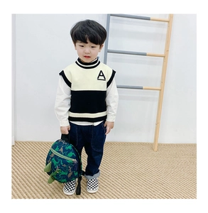 Détail d'un sac à dos dinosaure vert assorti à un gilet en tricot et un pantalon bleu enfant
