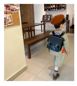 Classic black leather vintage satchel backpack worn by a child in a warm indoor setting