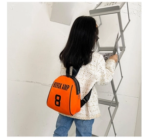 Detail of child wearing an orange letter-print backpack against a white wall