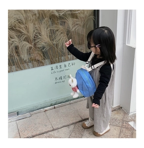 Side view of a light blue kids backpack featuring a cute white plush bunny charm pendant
