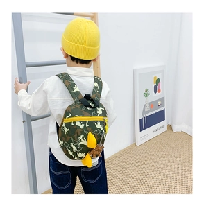 Détail du sac à dos dinosaure vert avec fermeture éclair jaune et pendentif peluche