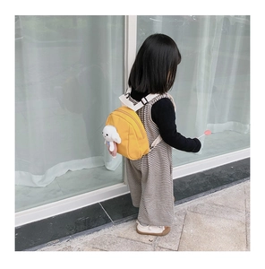 Detailed side view of a yellow canvas toddler backpack featuring a white puppy plush charm