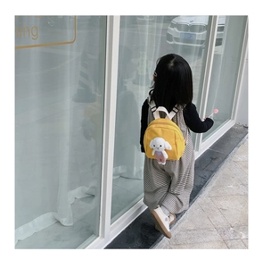 Toddler yellow backpack featuring a cute white plush lamb toy on a sunny street view