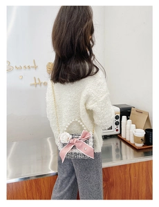 Detail of girls mini crossbody bag with pearl handle and pink bow in a cafe setting