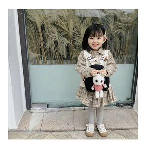 Detail of girls' plaid dress with beige vest and black backpack featuring a bunny pendant