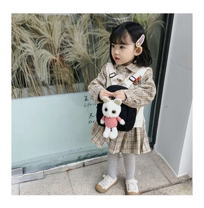 Detail of a kids black canvas backpack featuring a plush cat charm and wide straps