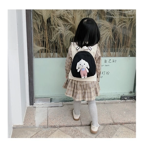 Rear view of a girl wearing a black canvas backpack with a cute white bunny plush toy