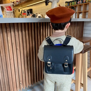 Vintage black PU leather kids backpack with double buckle straps in a cozy indoor setting