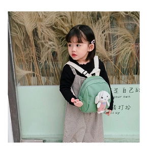 Toddler wearing a forest green canvas backpack with a cute plush bunny doll decoration