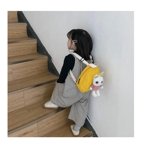 Rear view of a yellow toddler backpack with a white bunny plush doll on a young child