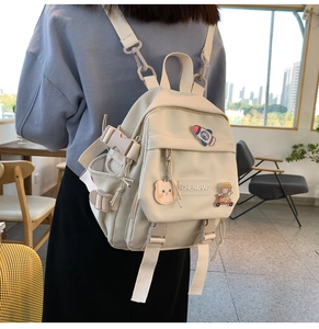 Détail d'un sac à dos crème avec des patchs de dessins animés et un porte-clé ours
