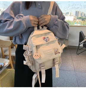 Détail du sac à dos beige pour école avec écussons de dessin animé et ours peluche